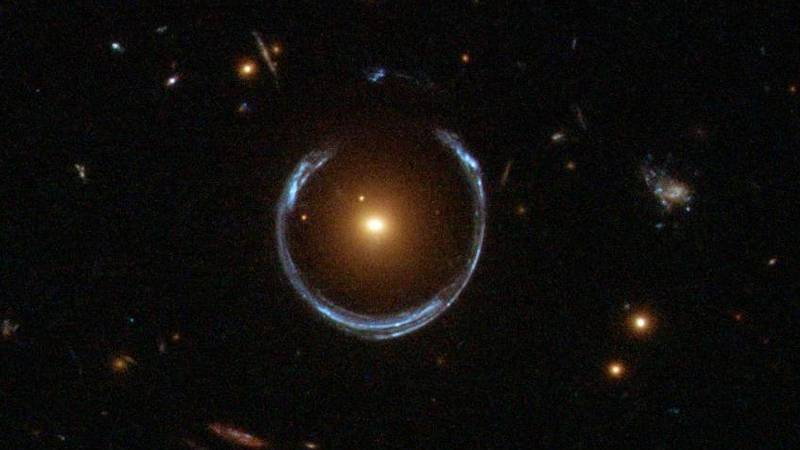A lente gravitacional da Ferradura Cósmica. O recém-descoberto buraco negro ultramassivo está localizado no centro da galáxia alaranjada. Muito atrás dela, uma galáxia azul está sendo deformada em um anel com formato de ferradura pelas distorções no espaço-tempo criadas pela imensa massa da galáxia alaranjada em primeiro plano. Crédito: NASA/ESA.